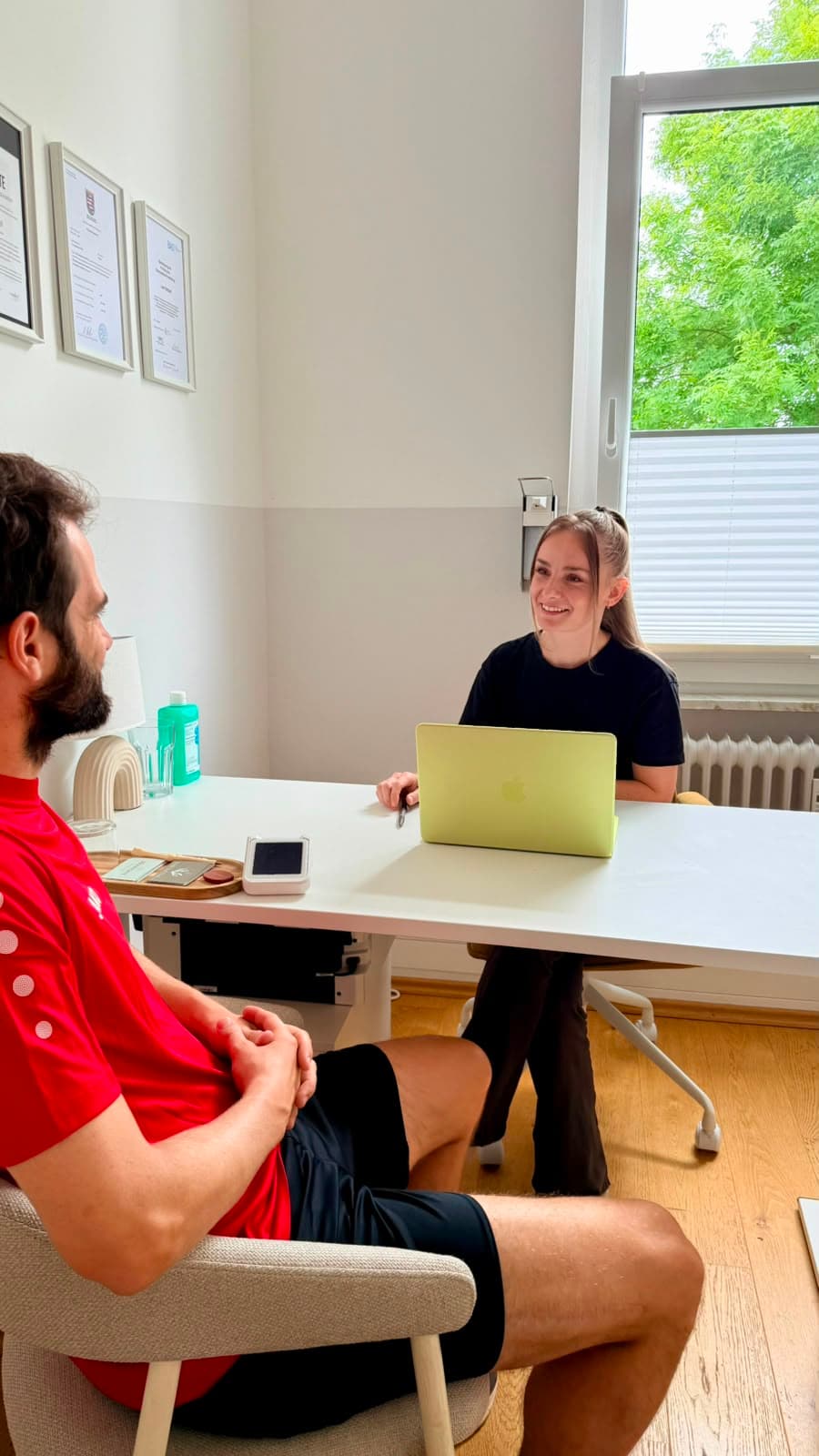 Michaela Schumacher im Gespräch mit einem Sportler am Schreibtisch ihrer Praxis.