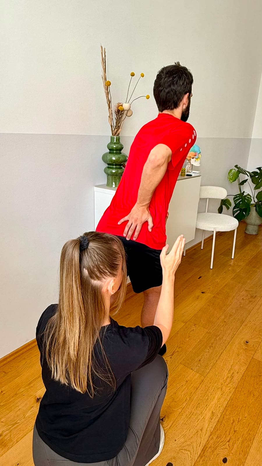Michaela Schumacher kniet hinter einem stehenden Sportler und korrigiert mit den Händen seine Haltung.